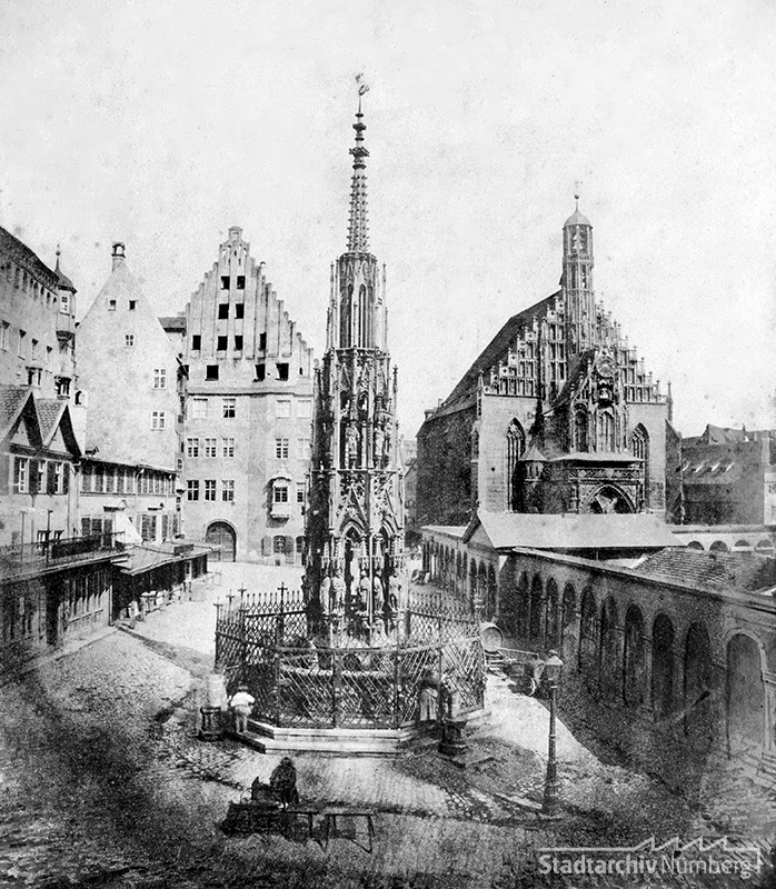 Der Schöne Brunnen von Westen mit der Frauenkirche im Hintergrund, dazwischen drängen sich die 1895 abgebrochenen Hauptmarkt-Kolonnaden. Um den Brunnen herum beleben gezeichnete Figuren die Architektur-Szenerie. (Stadtarchiv Nürnberg A 47-II-KS-134-23)